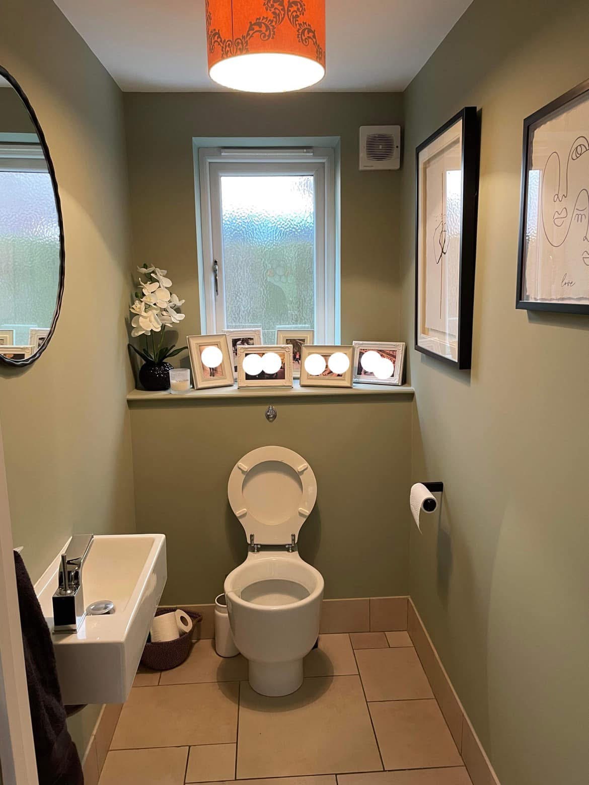 Finished cloakroom in sage green with a round mirror and line art on the walls