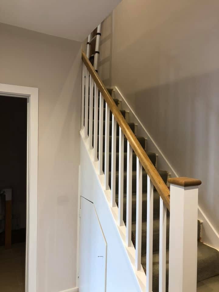Staircase with crisp white spindles and a warm stained handrail over grey carpet
