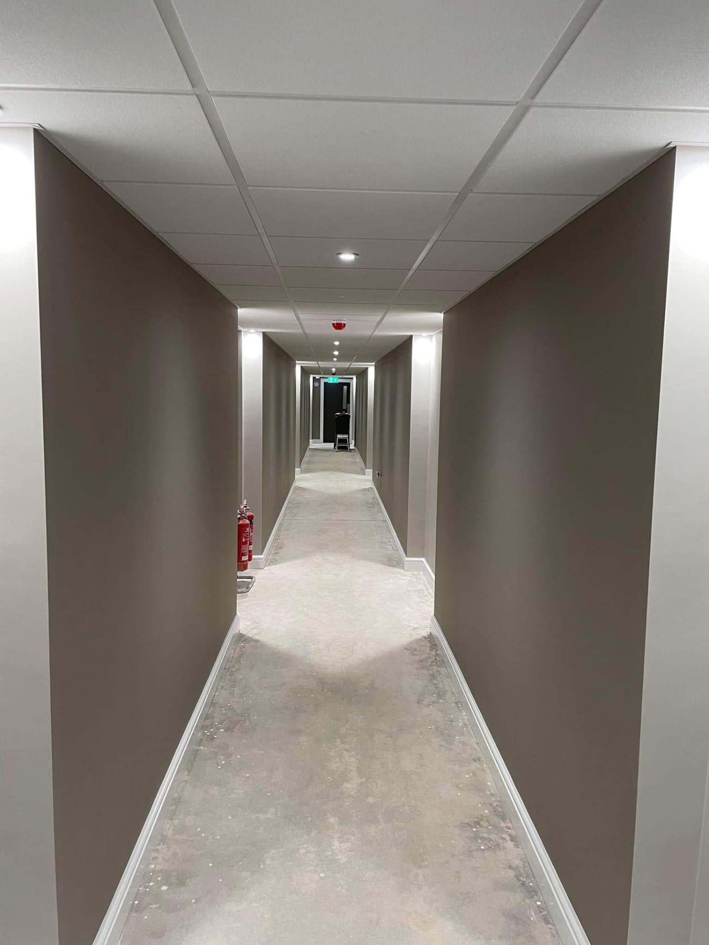 Finished long hallway with taupe walls, white skirting and a clean suspended ceiling