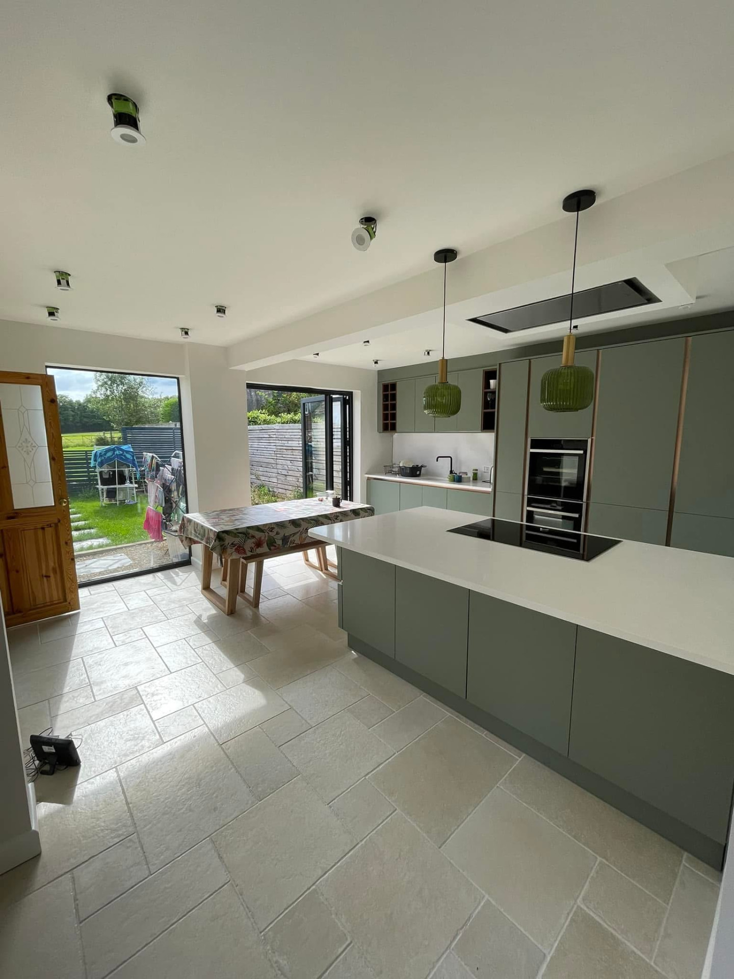 Finished kitchen with green cabinetry, white island and pendant lights over a tiled floor